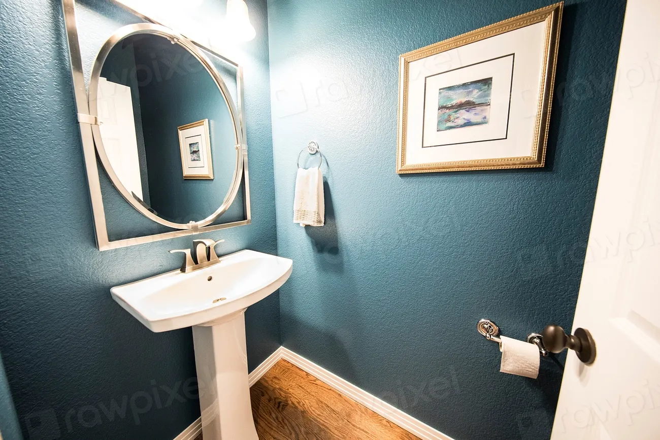 A small powder room with a pedestal sink against a teal wall